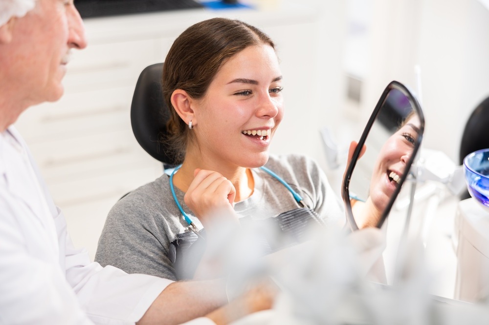 Dental patient smiling while viewing her smile in a hand mirror with her dentist